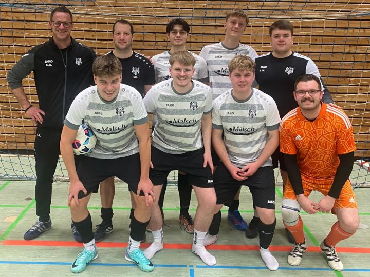 Neun Personen in Sportklamotten vor einem Fußball-Tor in einer Sporthalle